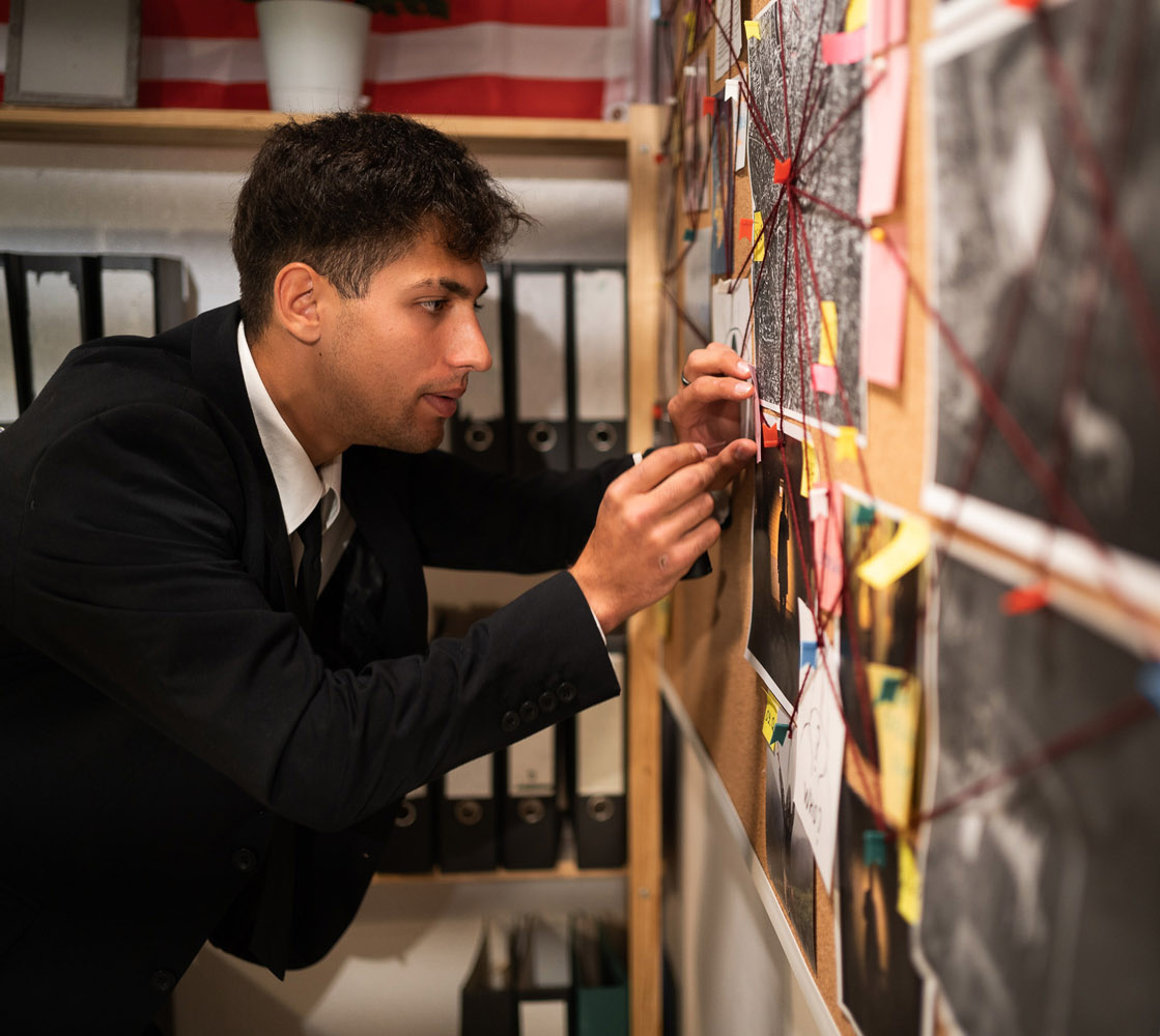 Man in black suit in front of board with string
