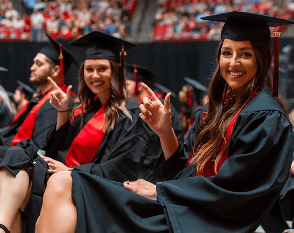 Texas Tech students in graduation attire smiling and making a guns up gesture.
