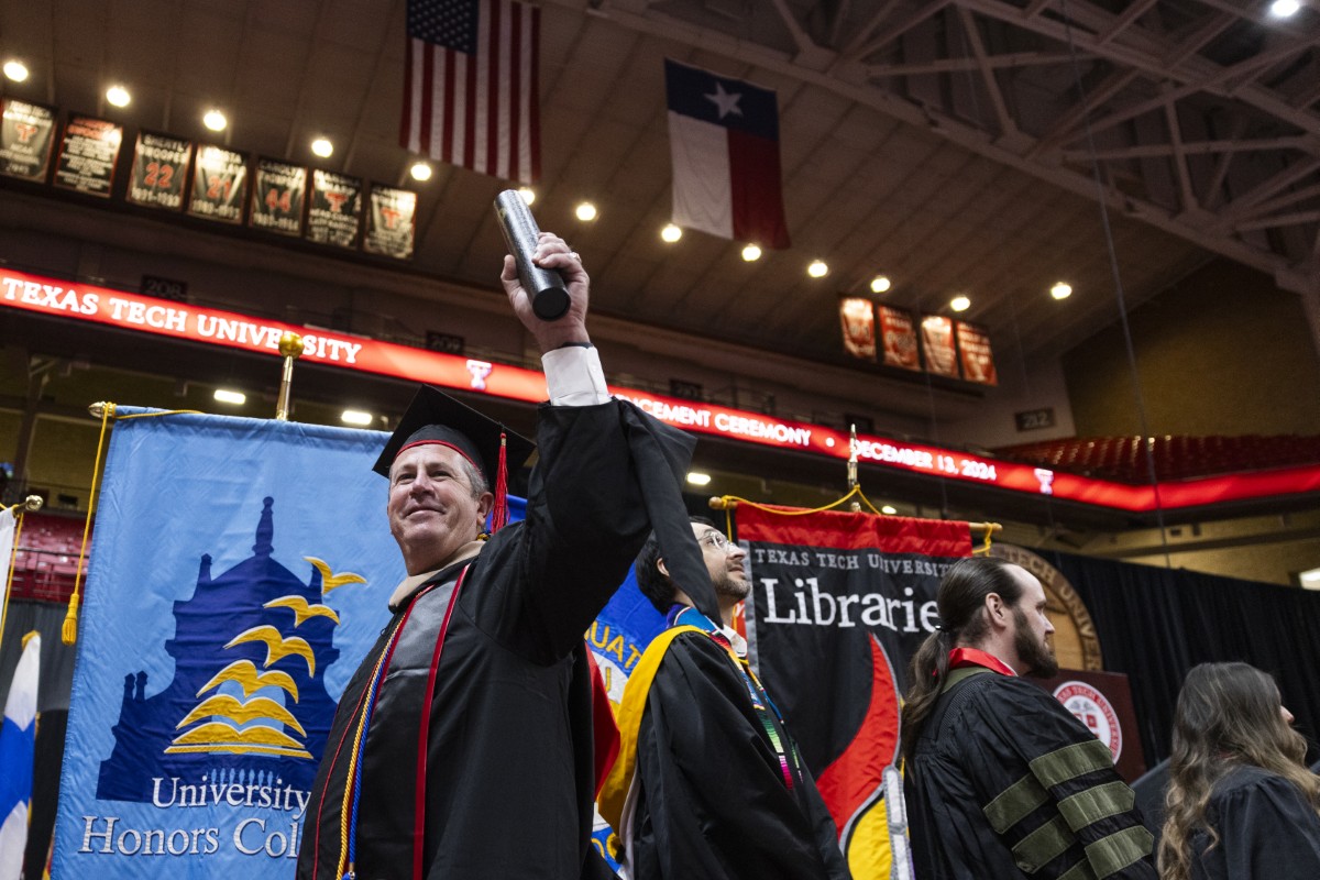 Person in graduation robes holds up diploma at ceremony.