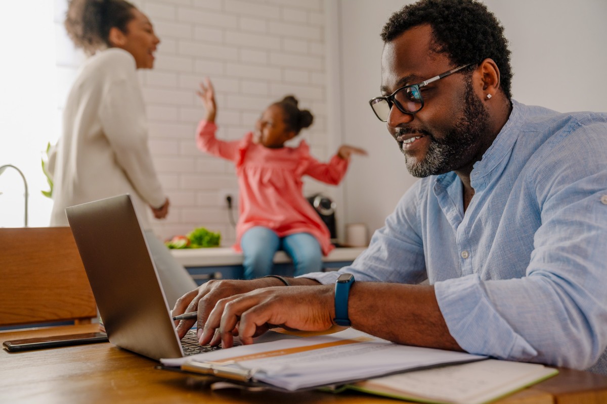 Parent works from laptop with children in background.