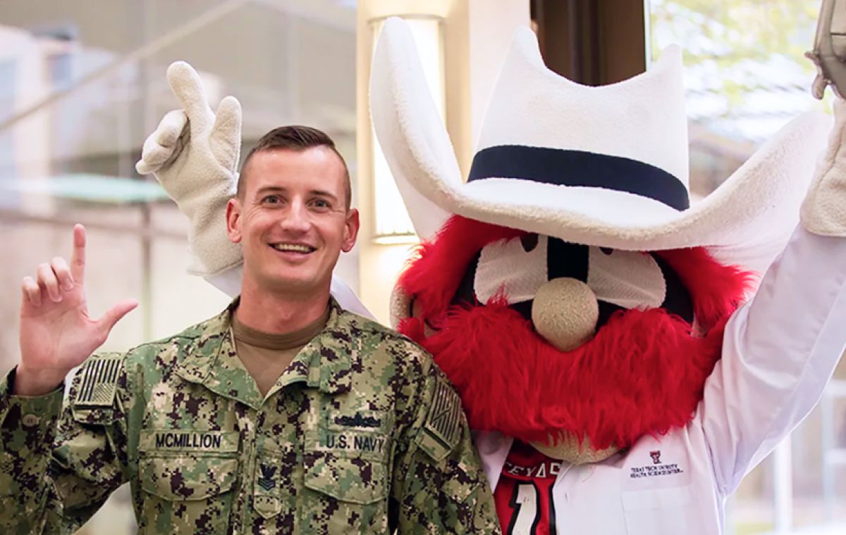 U.S. Navy officer in a camo uniform standing next to the Texas Tech University mascot, Raider Red, both making the gun's up gesture.
