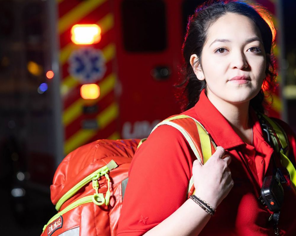 A female parametic standing in front of an ambulance at night.
