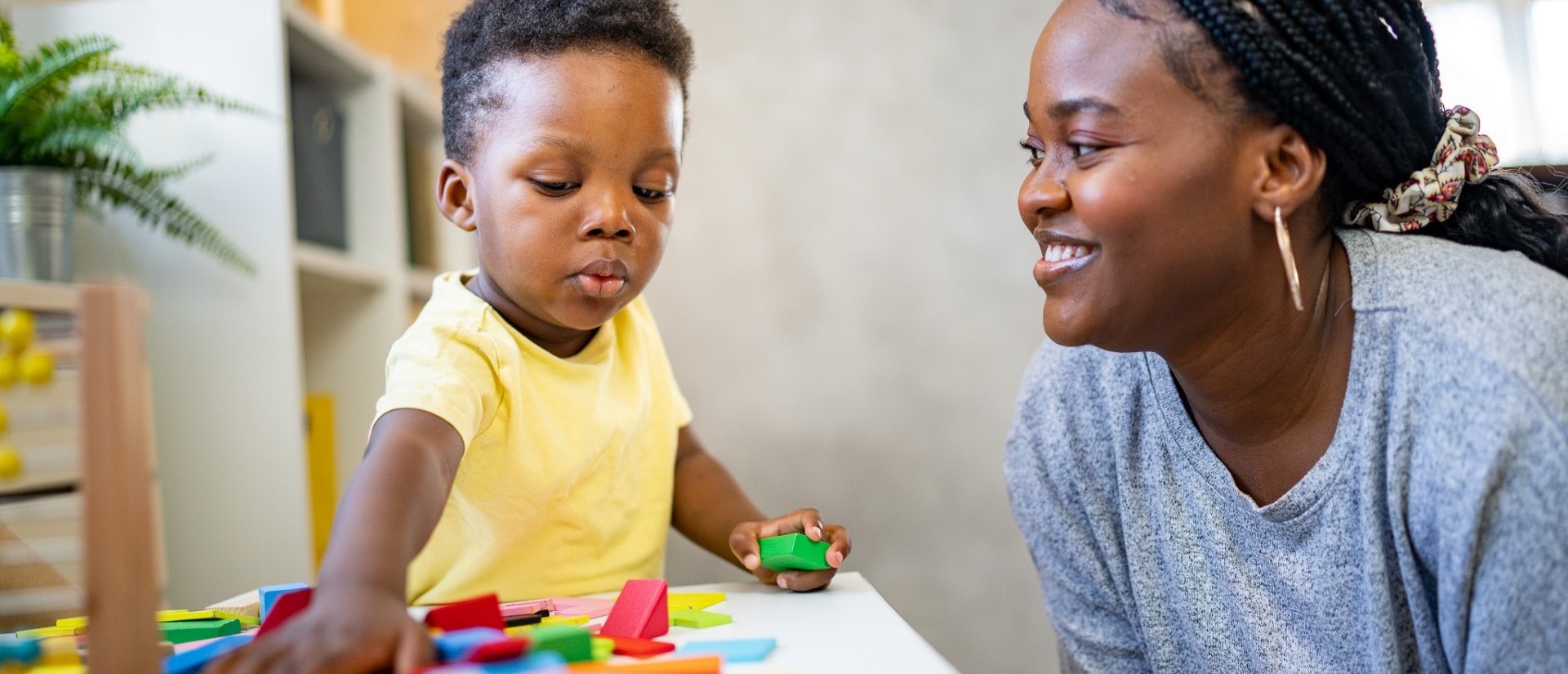 Photo of a smiling woman and child playing with blocks.