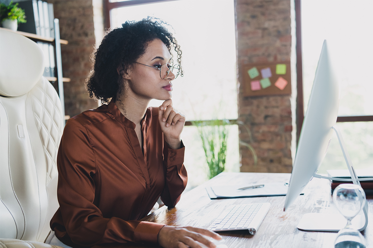 Woman wearing glasses working at a computer inside a brick building office space. 