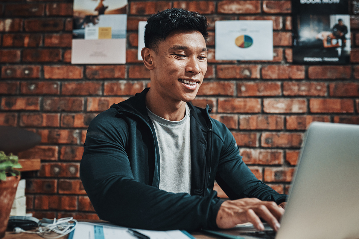 Man in athletic wear working on a computer with fitness images displayed in the background.