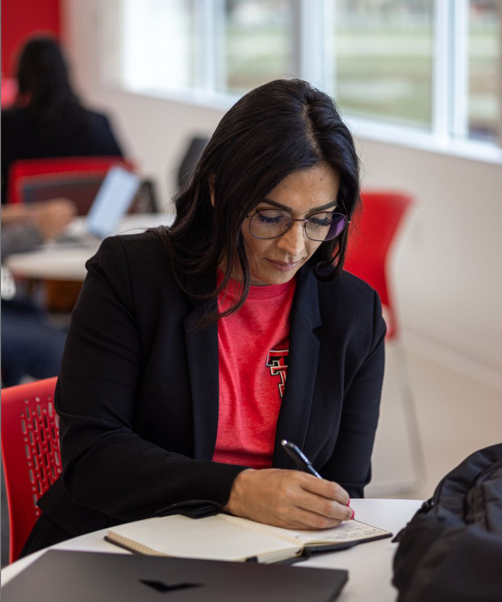 A woman wearing a red texas tech shirt writing in a notebook.