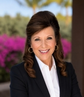 photo of woman with dark hair wearing a dark suit with a tropical background
