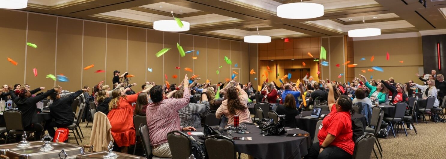 Colorful paper airplanes flying in a confrence room as people throw them.