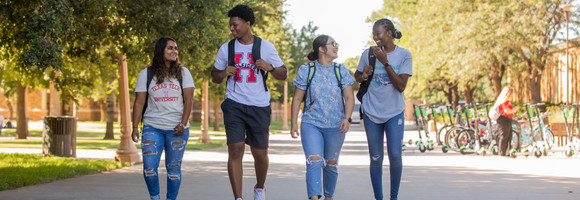 Four students with backpacks walking on campus, looking at each other and smiling.