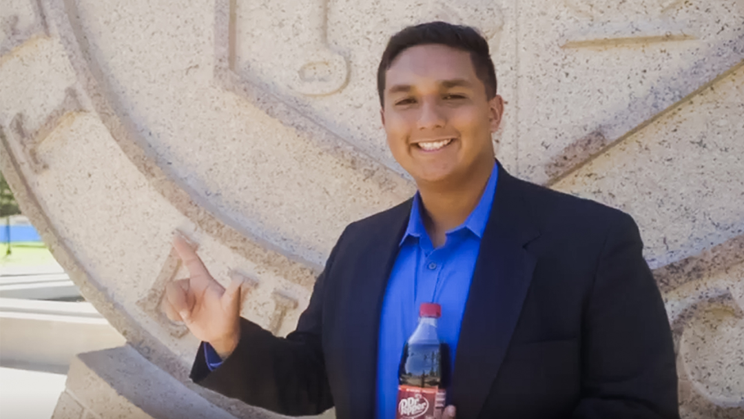 Patrick Herrera standing in front of the Texas Tech University seal with a Dr Pepper bottle. 