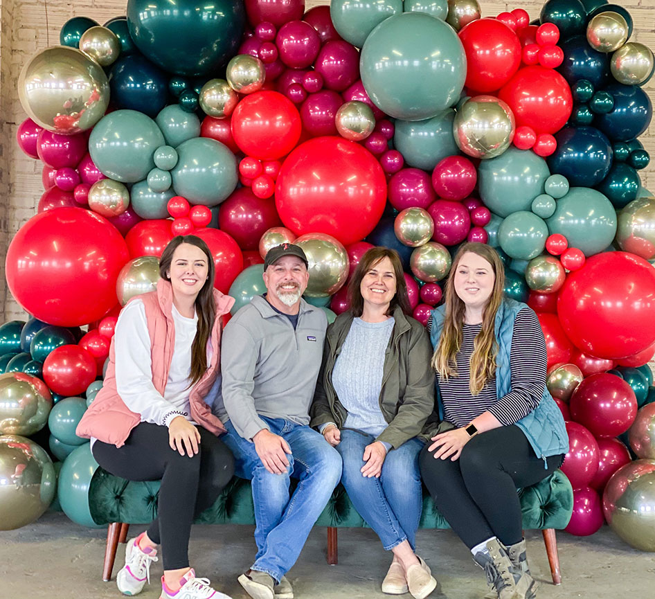 Jon (father), Penny (mother,) and Sydney (sister) — sit in front of one of their balloon installations.