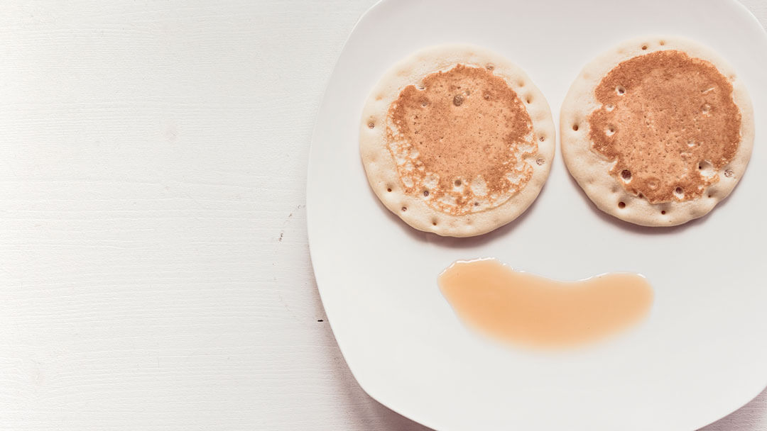 A plate with two small pancakes and a small amount of sauce beneath them forming a "smiley" face.