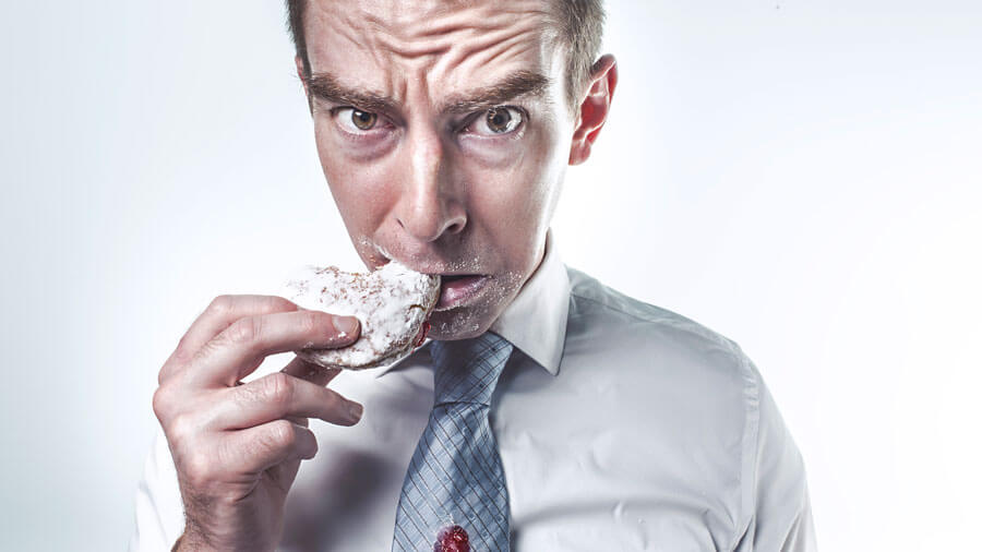 A man with the area surrounding his mouth covered in powdered sugar from the pastry he is eating.