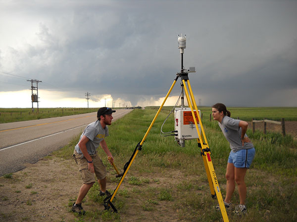two students setting up sticknet with tornado in background