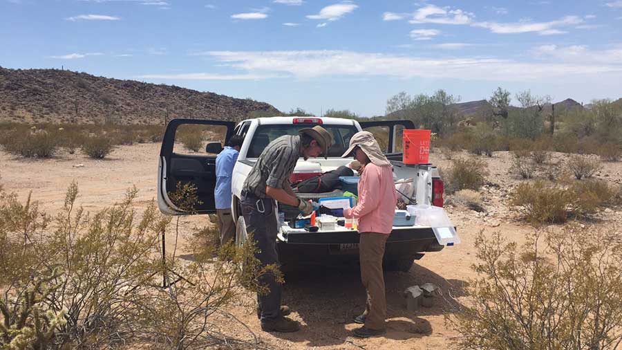 man and woman testing water on back of white pickup truck in the middle of the desert