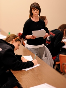 A female professor passes out notes to a students sitting at a table in the classroom.