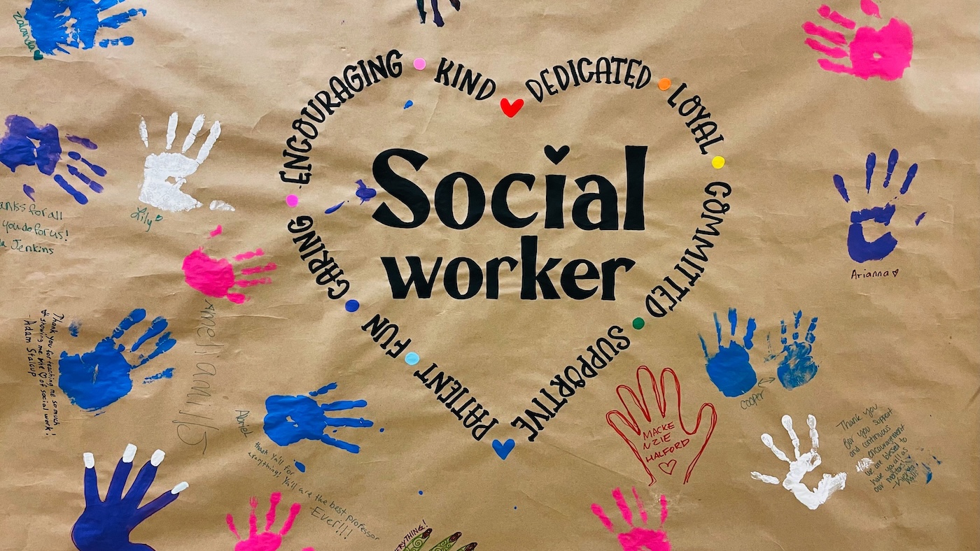 A poster reading social work is covered in the imprints of students’ hands in colorful paint