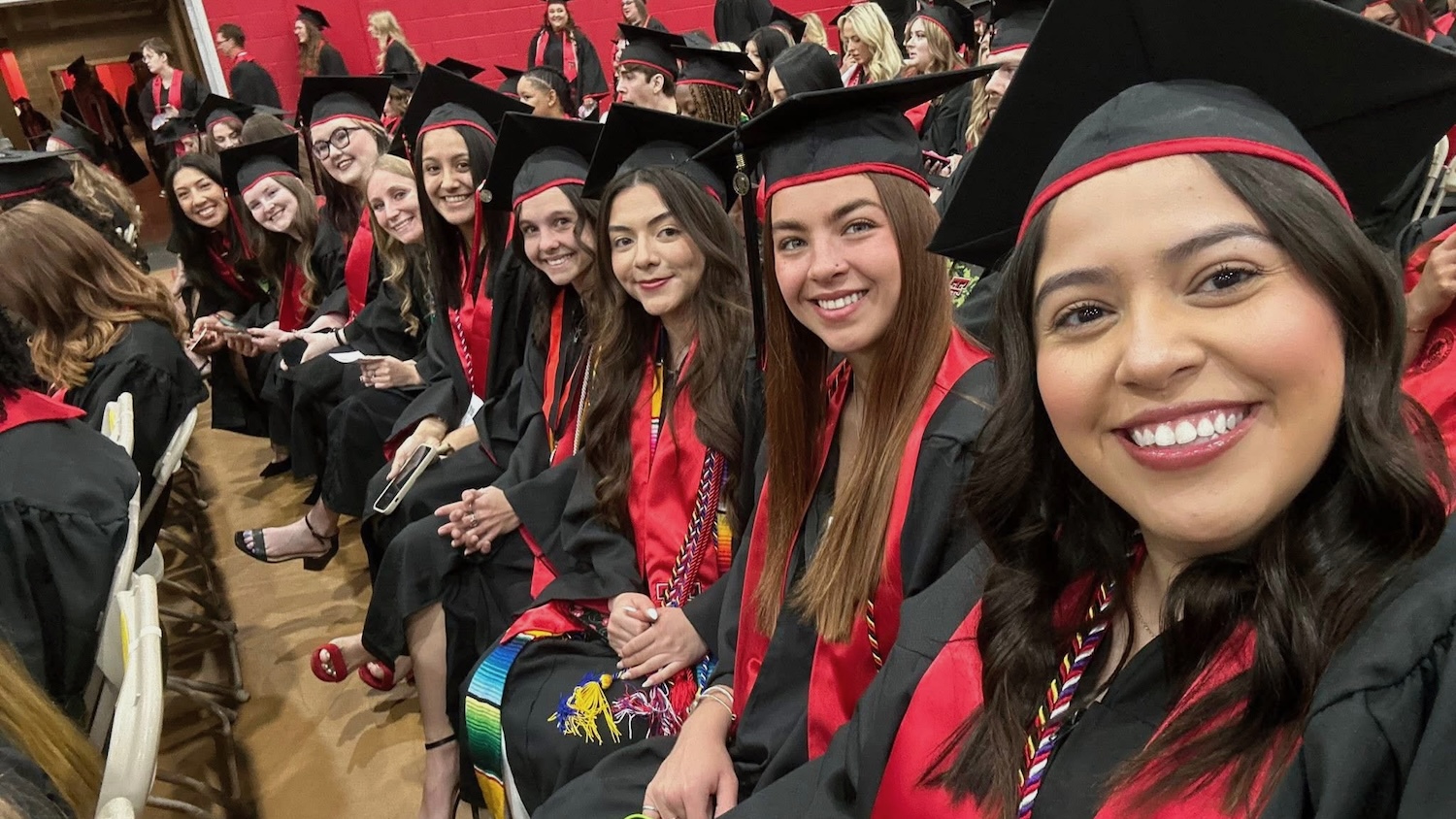 students in regalia seated in a row look towards camera and smile 