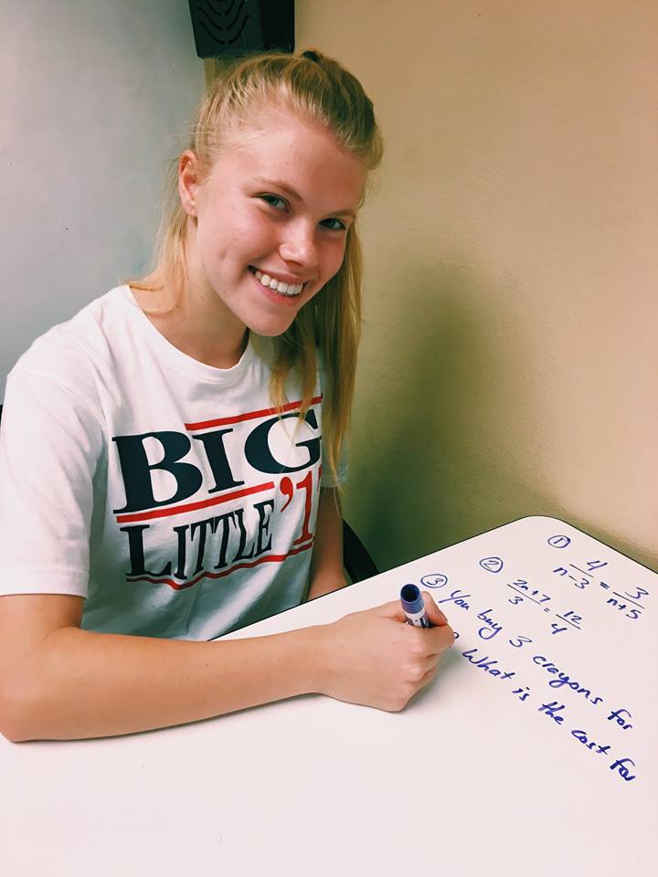 Smiling blonde young lady writes math problems on a dry erase board