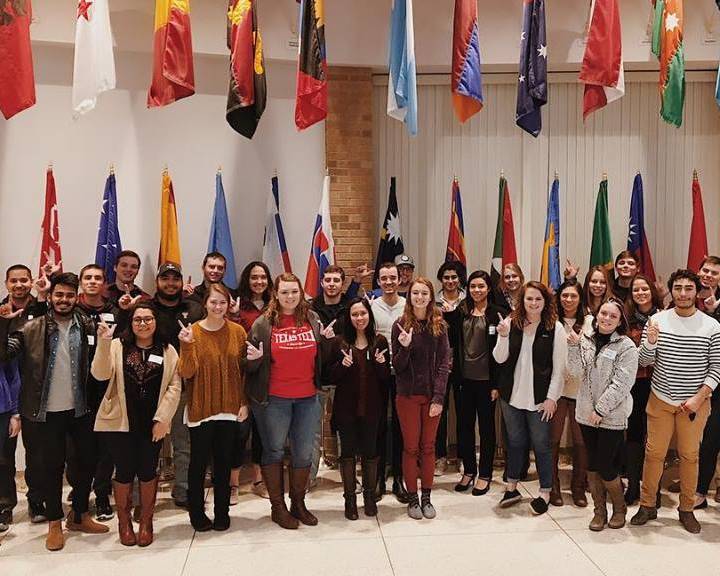 Tutor trainees stand in a group under various flags at the International Cultural Center