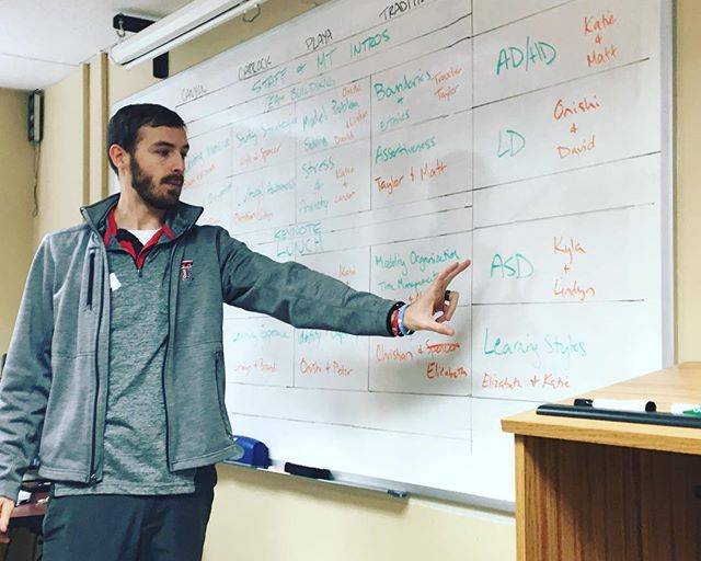 Taylor Fortney, a young white man with brown hair and beard, points at a chart on a whiteboard