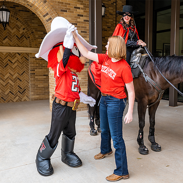 Veterinary students high fiving Raider Red with the Masked Rider behind them