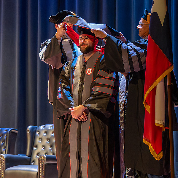 Veterinary student in graduation regalia being hooded by two faculty members