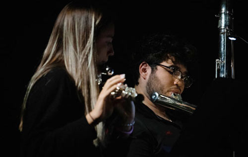 Students playing a flute in front of microphone